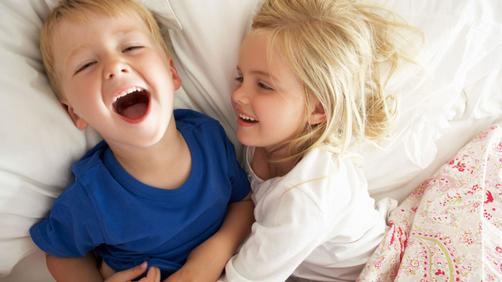 two children laugh after snoring in bed